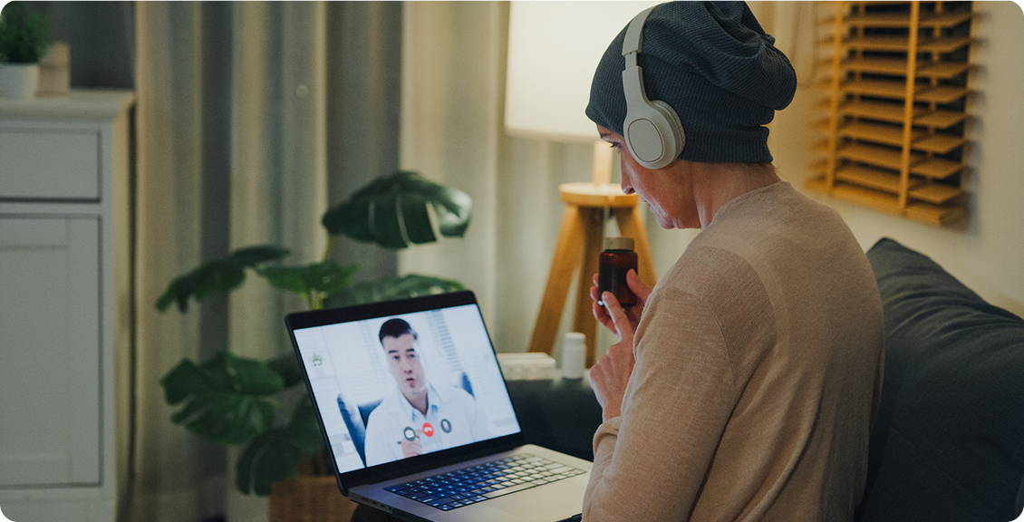 Person wearing headphones joins a video call on a laptop in a cozy living room, holding a smartphone; warm, quiet, connected mood.